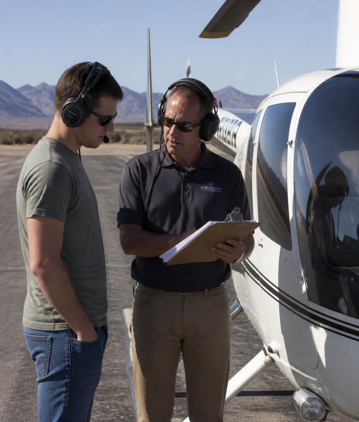 A flight instructor briefing a student beside a training helicopter on a desert ramp
